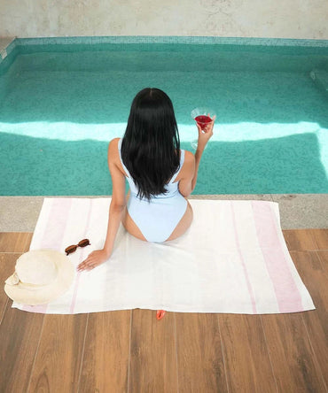 Woman sitting by a pool holding a glass of red wine on a towel.