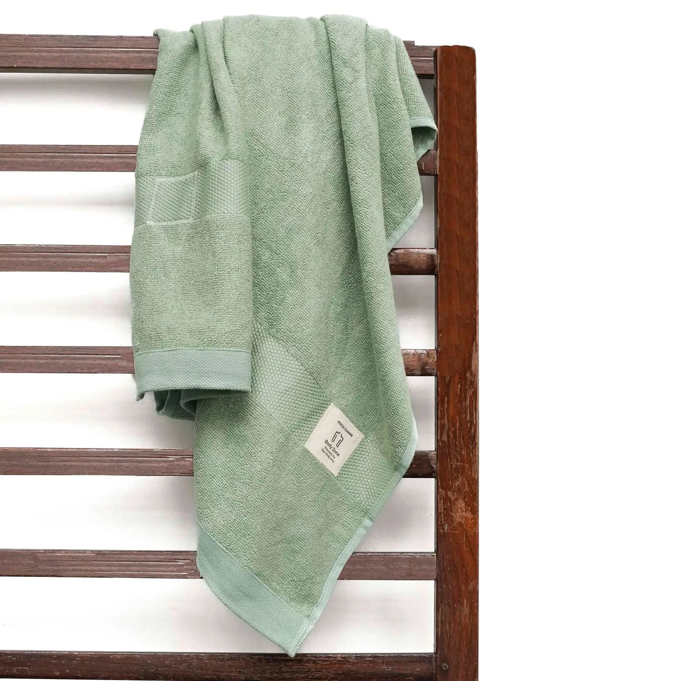 Sage green towel hanging on a wooden towel rack with a white background